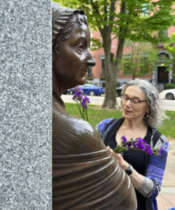 Photograph of bronze statue of a woman, with live woman placing purple flowers into statue's hand.