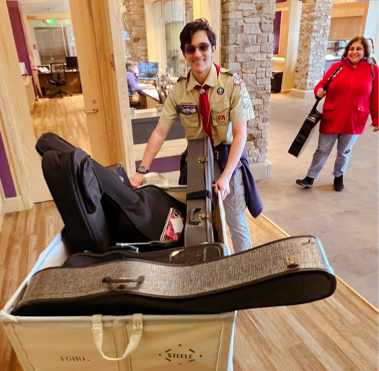 Photograph of Boy Scout in uniform pushing a load of musical instruments.