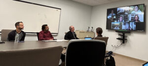 people at a conference room table and big-screen monitor