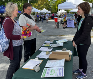 Attendees at a Farmers Market stand before informational paperwork on a table.