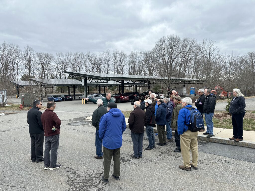 A group stands outside with solar panels mounted on a canopy in the background