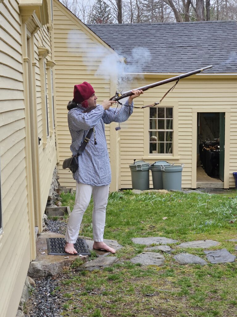 Barefoot man wearing a red nightcap firing a musket.