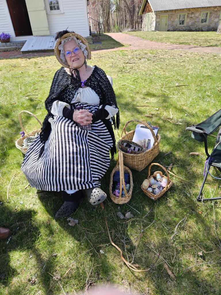 Woman in revolutionary era garb with baskets of yarn and other oddments.