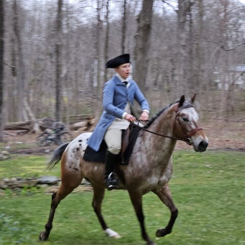 Man in a blue revolutionary era coat and tricorner hat riding a horse.